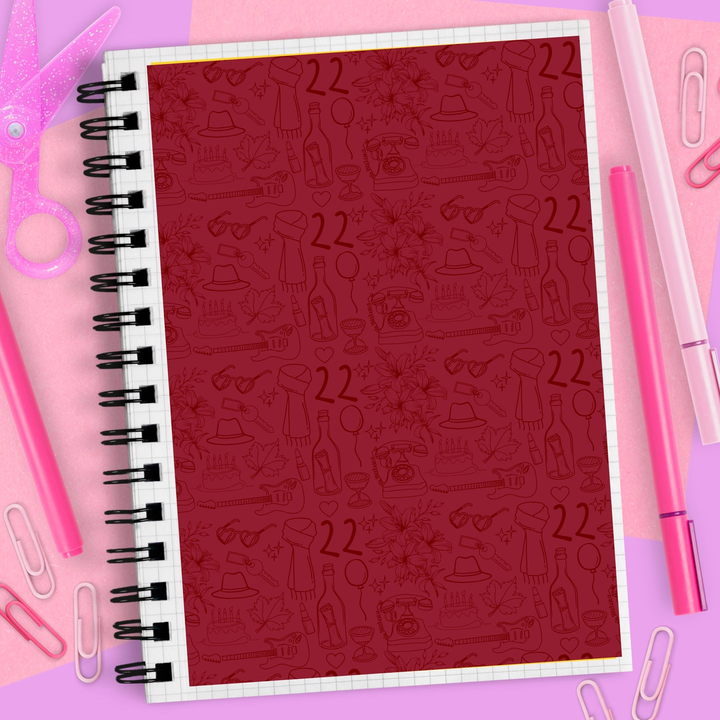 Notebook with red cover featuring black illustrations and '22' on a pink background with stationery items.