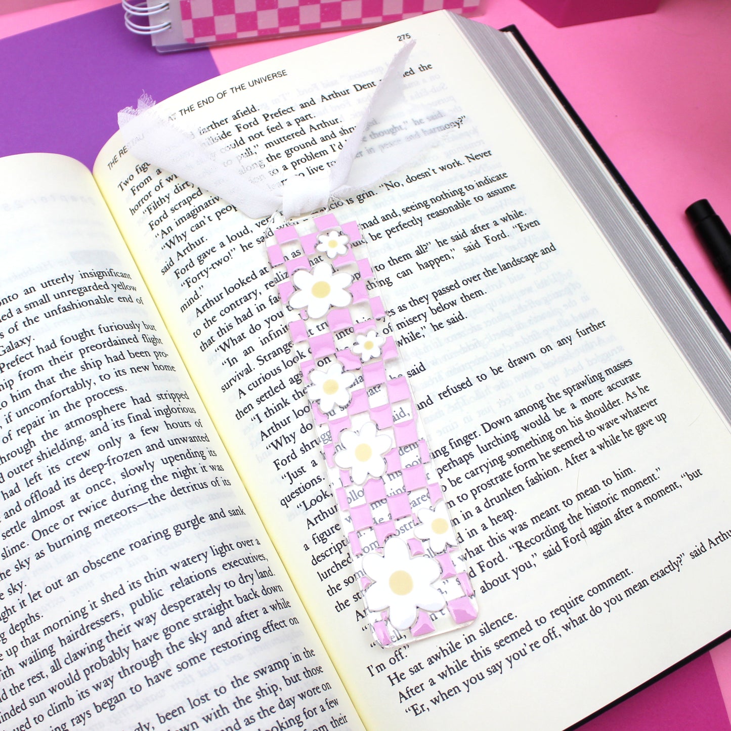 Decorative floral bookmark on an open book with a pink checkered background