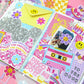 Colorful stationery items including cards, stickers, and envelopes on a pink background.
